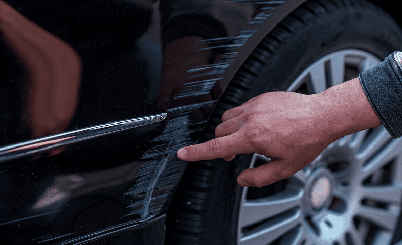 Hand pointing at scratched car surface